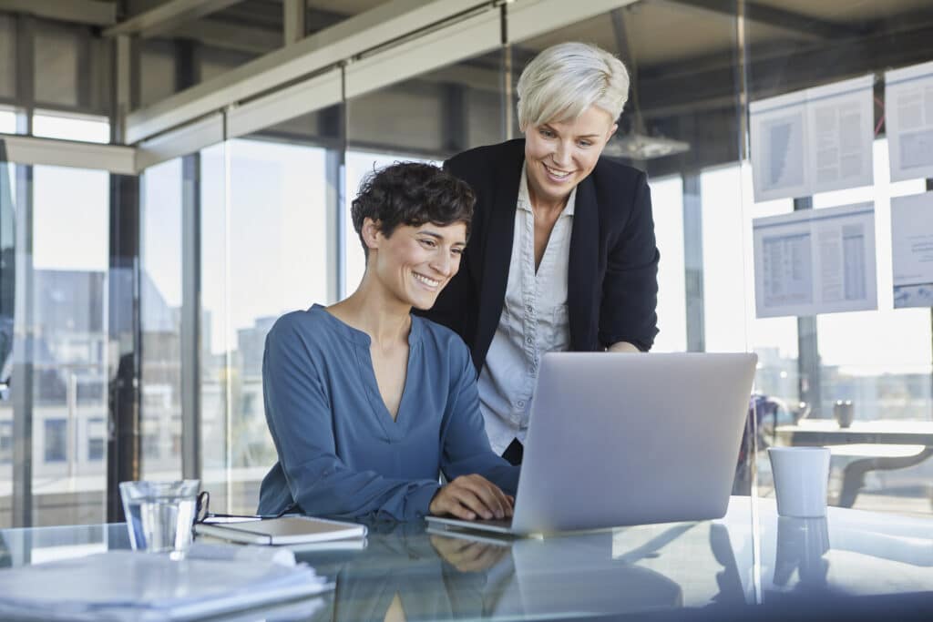 two smiling businesswomen sharing laptop at desk i 2022 12 16 22 12 07 utc